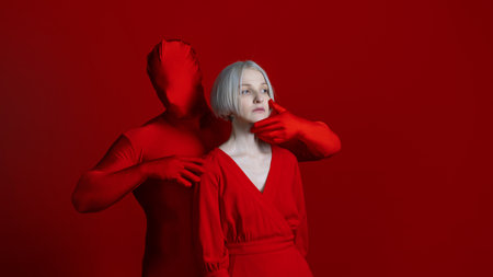 A part of me, individual or imposed from the outside. Something from the inside and something from the outside as parts of a single personality, a concept. A woman in a red dress and a faceless character in red touches her with his hands, photo on redの写真素材