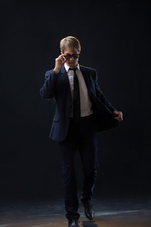 confident man strides forward in a dark suit, exuding authority and professionalism. The low-key, dark background highlights the formal attire in a corporate settingの写真素材