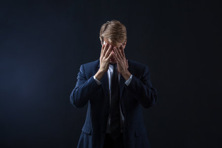Headache and stress at work, concept. a young businessman suffers and clutches his head with his hands squeezing the bridge of his nose. Overwork and professional burnoutの写真素材