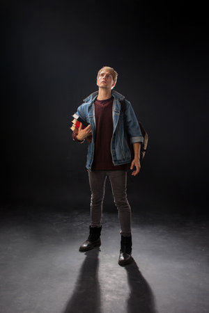 person stands confidently wearing a denim jacket over a maroon sweater, holding a blue jacket in a studio with a dark, atmospheric background. Casual and stylish look.の写真素材