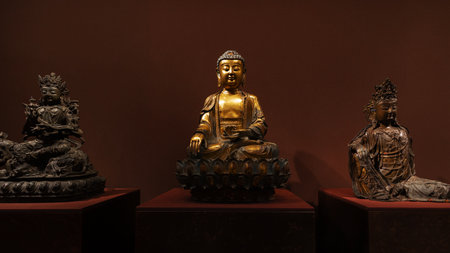 A museum exhibit of an antique three Buddha sculpture in the lotus position, representing enlightenment and nirvana. The stone or bronze statuette, possibly gilded, showcases Buddhist history and culture.の写真素材