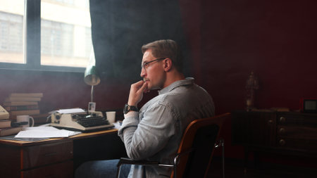 Vintage-style writer immersed in work, surrounded by smoke in softly-lit cinematic office setting.の写真素材