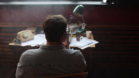Cinematic vintage journalist scene - young writer smokes while struggling with article at typewriter.の写真素材