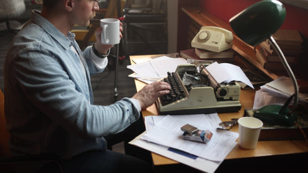 A male journalist smokes and writes his article intensely. Vintage-style office, cinematic style and soft focus. A young man experiences difficulties and frustration while doing literary workの写真素材
