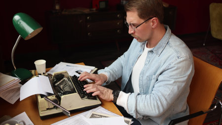 Cinematic writer scene - young man thinking at vintage typewriter, soft-focus on smoky paper-filled office.の写真素材