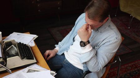 Writer in creative thought at vintage typewriter, cinematic soft-focus on smoky paper-strewn office scene.の写真素材