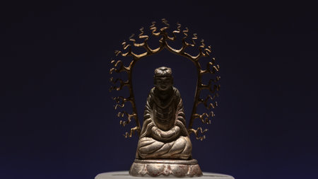 An antique Buddha sculpture in the lotus position, symbolizing enlightenment and nirvana. The stone or bronze statuette, possibly gilded, is displayed in a museum, reflecting Buddhist history and culture.の写真素材
