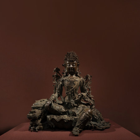 A museum display of an antique Buddha sculpture in the lotus position, representing enlightenment and nirvana. The stone or bronze statuette, possibly gilded, highlights Buddhist history and cultural heritage.の写真素材