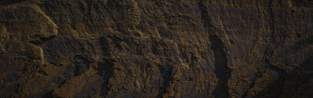 A textured stone background with chiaroscuro lighting, showcasing a brutal, monolithic rock formation. Cracks and fragments highlight its geological power, perfect for design templates or science-themed projects.の写真素材