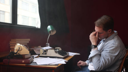 A male writer writes an article or novel at his desk in his office. The author experiences frustration and the pangs of creativity, a soft cinematic image, a soft focus.の写真素材