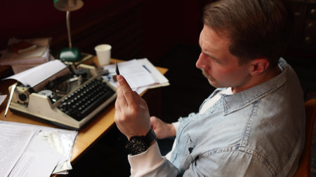 Writer in creative thought at vintage typewriter, cinematic soft-focus on smoky paper-strewn office scene.の写真素材