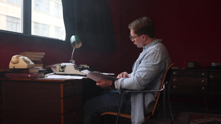 Male writer immersed in book work at vintage desk, smoky office atmosphere captured in cinematic soft focus.の写真素材