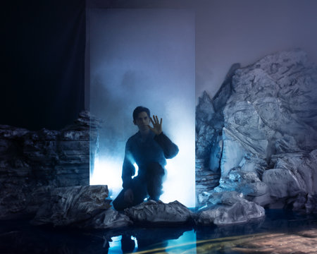 A man in overalls, an explorer in an ice cube with smoke, landing on another planet or being in a dangerous environment. A cold landscape with rocks covered with ice. A fantastic concept of exploring other worlds, teleportation, survival in a hostile environment and isolation from the outside atmosphere. Cinematic picture in the fogの写真素材