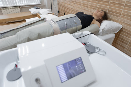 Female client receiving pressotherapy treatment in a spa, modern detox machine for lymphatic...