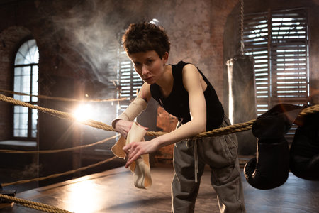A woman in a boxing gym, portrait by the ropes, cinematic style, dark tones. Training and overcoming...