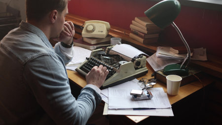 Male writer deep in thought at vintage typewriter, cinematic soft-focus on smoky office filled with papers.の写真素材