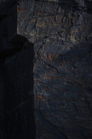 A textured stone background with chiaroscuro lighting, showcasing a brutal, monolithic rock formation. Cracks and fragments highlight its geological power, perfect for design templates or science-themed projects.の写真素材