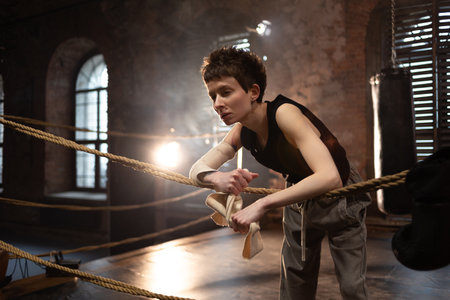 Female fighter resting between rounds, leaning on ropes with intense cinematic look.