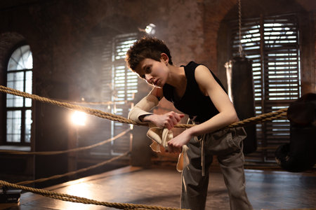 A woman in a boxing ring, wrapping an elastic bandage around her arms, preparing for boxing training. The photo is in a cinematic style, the light gives the mood to a sports motivational story about self-improvement and the path to the goalの写真素材