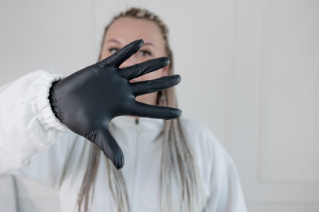 Beauty salon worker in white uniform and black gloves displays open palm by face