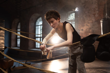 A woman in a boxing gym, portrait by the ropes, cinematic style, dark tones. Training and overcoming oneself, motivationの写真素材