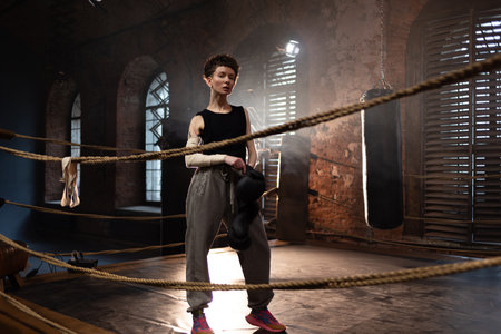 A woman in a boxing gym, portrait by the ropes, cinematic style, dark tones. Training and overcoming oneself, motivationの写真素材