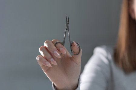 Close-up of manicure scissors in professional hand working on stylish beige manicure.