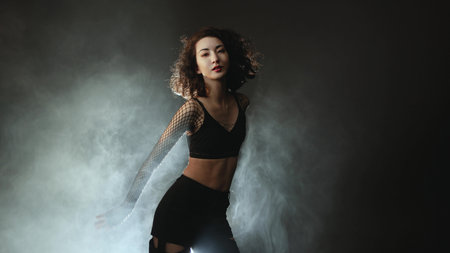 Modern dance solo: woman in black pants and sheer blouse moving gracefully through dramatic smoke lightingの写真素材