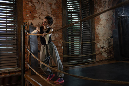 Short-haired boxer pausing workout, leaning on ring ropes with cinematic intensityの写真素材