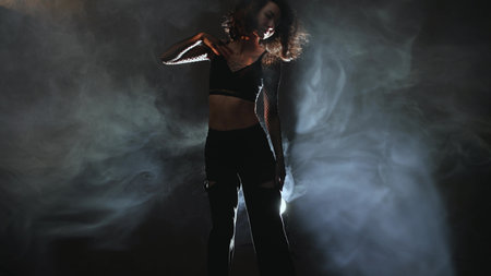 Contemporary dance artistry: female performer in fashionable outfit dancing through atmospheric hazeの写真素材