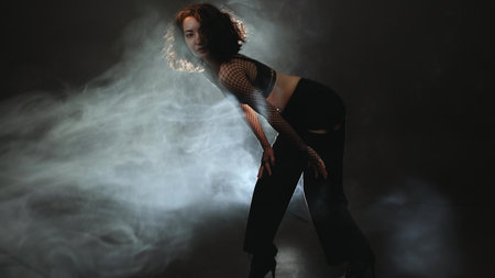 Contemporary dance artistry: female performer in fashionable outfit dancing through atmospheric hazeの写真素材