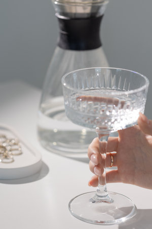 An elegant girl holds a glass of clean water in her hands, a hand with an elegant light manicure, a...
