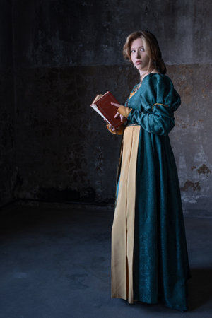 A noble lady in an emerald Renaissance dress with a book in her hands. A young blonde in a medieval costume, portrait on the background of a stone castle wallの写真素材