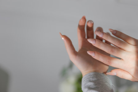 Elegant almond nails with beige gel polish, close-up of glamorous feminine hands in soft light.の写真素材