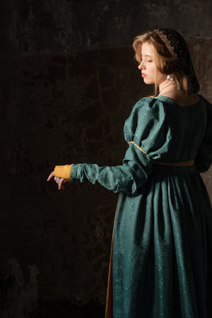 Fantasy portrait: fair maiden in lush green Renaissance attire leaning against textured castle wallの写真素材