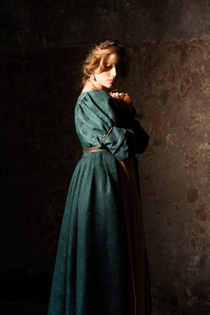 Radiant blonde in ornate green historical dress, medieval-style portrait with stone wall backgroundの写真素材
