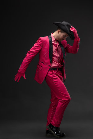 Young man in all-pink rhinestone suit, doll-like glamorous kitsch style on gray. Dancing in a cowboy hatの写真素材