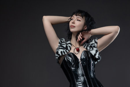 Gothic fashion: girl in glossy corset with checkered skirt, assertive pose on grayの写真素材