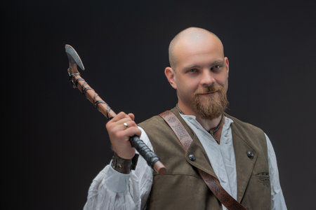 Bald man as wealthy medieval figure in white blouse and vest holding battle axeの写真素材