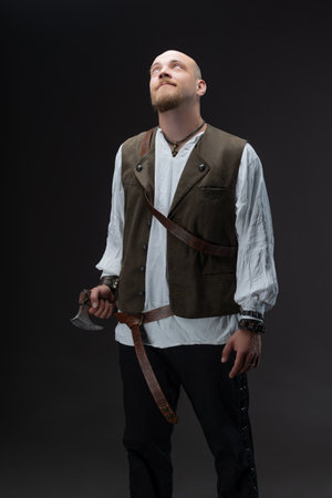 Bald male model as affluent medieval inhabitant with battle axe on studio gray