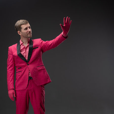 Totally pink outfit, a young man in a stunningly bright and daring suit in a completely bright crimson color, pink shirt and jacket with trousers covered with rhinestones, doll-like glamorous kitsch style, photo on a gray backgroundの写真素材