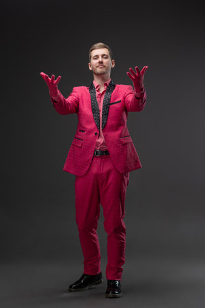 Young man wearing daring all-pink suit with rhinestones, kitsch style on gray, Sends everyone an air...