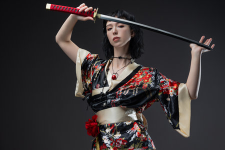 Beautiful model combines traditional Asian aesthetics with cyberpunk fashion in short kimono outfit, wielding katana against plain gray backdrop.の写真素材