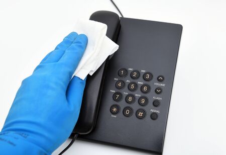 Worker's hand wipes dust and dirt on a landline phone. A maid or housewife takes care of the house. General, regular cleaning. The concept of a commercial cleaning companyの写真素材
