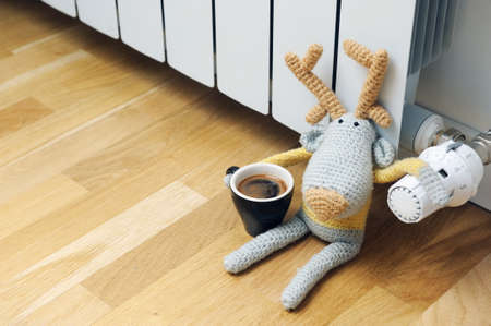 Knitted deer sits on the radiator with a cup in his handの写真素材