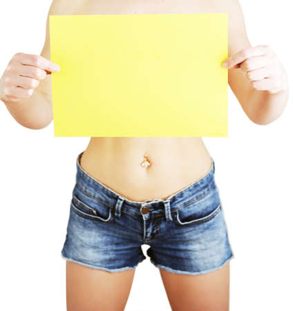 Slender cute young girl with long curly hair in blouse and blue jeans holding one bright yellow sheet of paper standing on yellow background vertical pictureの写真素材