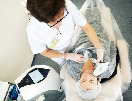 Belarus, Minsk-October 31, 2019: Multifunctional platform Viora V30. Woman receives laser and ultrasound treatment of face and body and hands in a medical sanatorium, skin rejuvenation concept.のeditorial素材