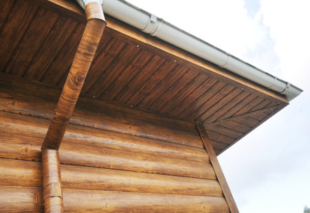 Roof made of metal with a gutter and a drainpipe. Log house with a roof made of iron tiles and a...