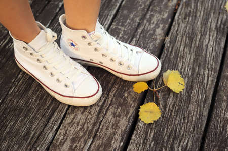 Belarus, Minsk - June 27, 2019: a girl in white cloth Converse sneakers stands in the autumn forest on a wooden bridge.のeditorial素材