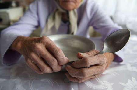 View from above.The hands of an old grandmother of 90 years are holding an empty aluminum bowl and spoon, poverty and poverty, the hunger of the older generation.の写真素材